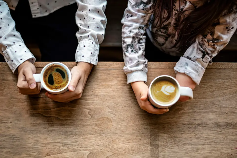 Two people holding coffee cups at a wooden table