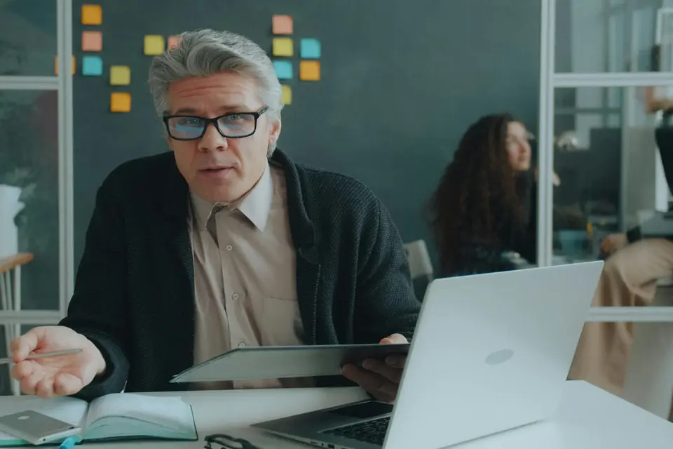 Gray-haired man with glasses explaining something on a tablet