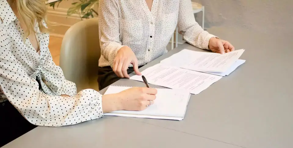 Zwei Frauen sitzen an einem Tisch, Unterlagen