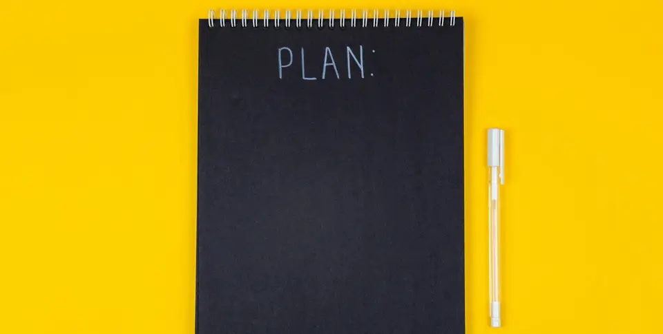 Notizblock mit Schriftzug "Plan" auf gelben Hintergrund mit weißem Stift