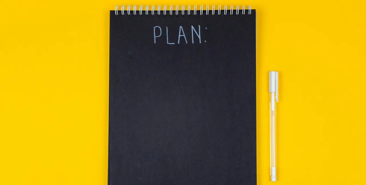 Notizblock mit Schriftzug "Plan" auf gelben Hintergrund mit weißem Stift
