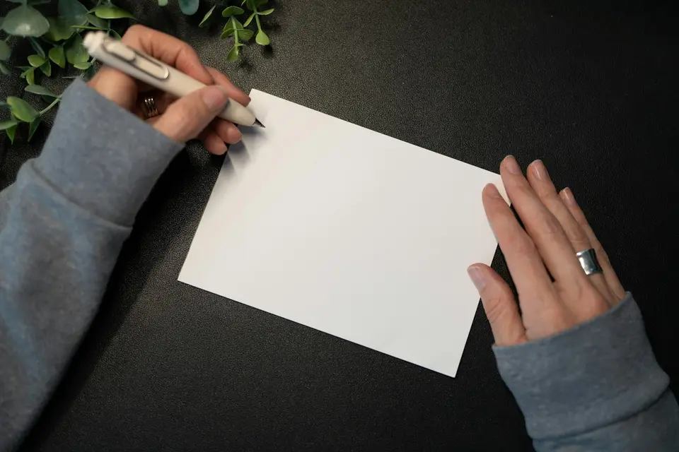 Hands writing on a blank greeting card with greenery