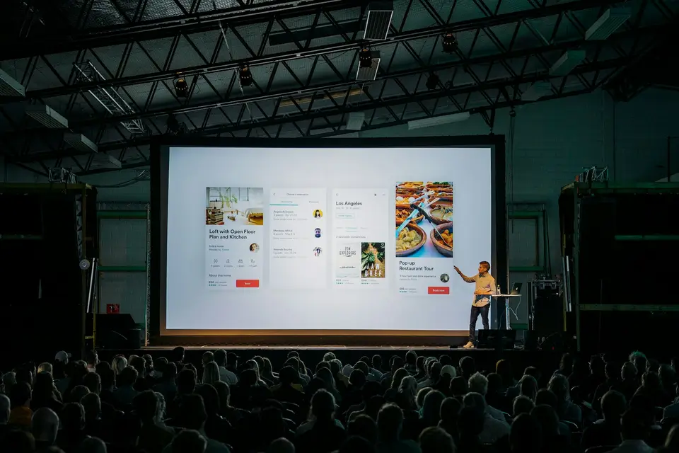 Speaker presenting in front of a large screen to an audience