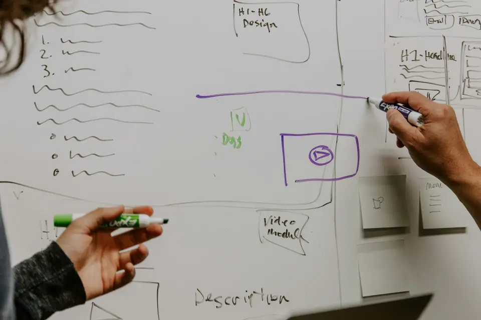 Zwei Personen skizzieren an einem Whiteboard eine Struktur mit Kästen und Listen