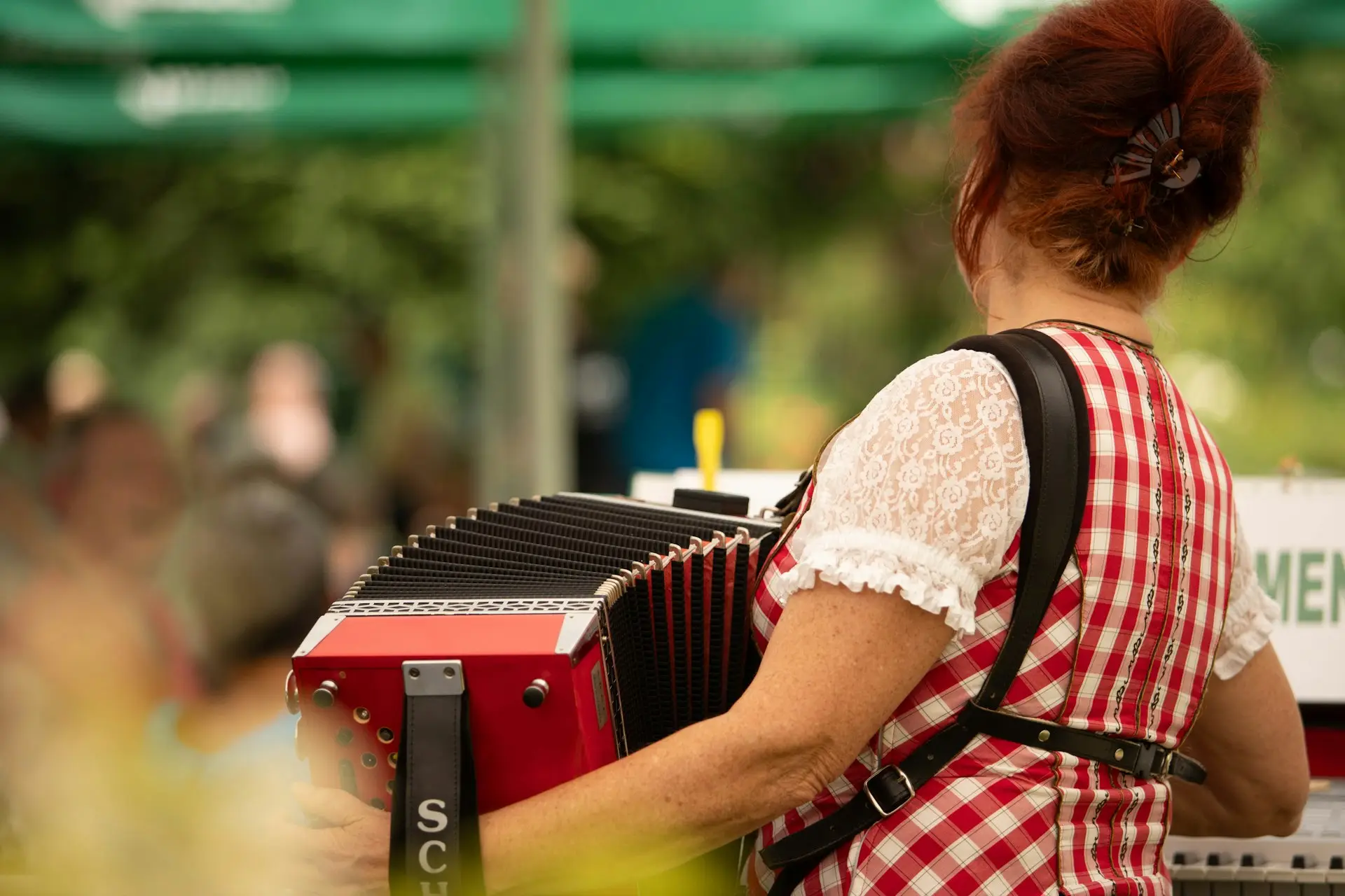 Frau im rot-weiß karierten Kleid spielt Akkordeon bei einem Fest