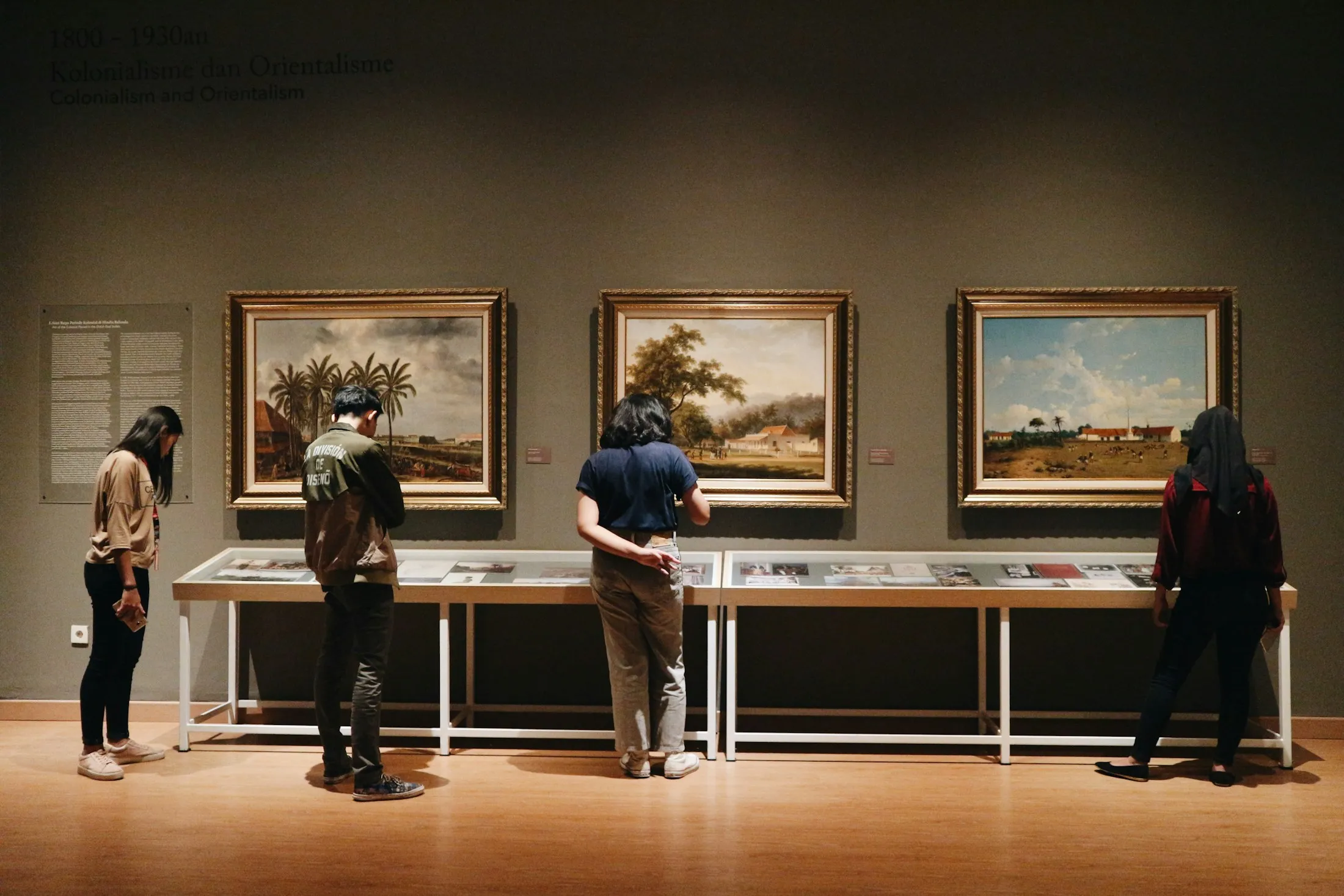 Visitors looking at landscape paintings in a museum gallery.
