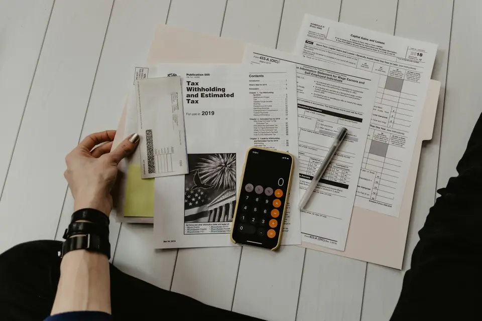 Person hält ein Blatt Papier neben Stift und Taschenrechner