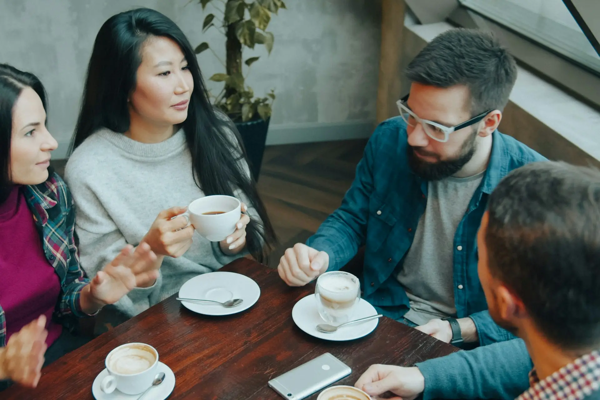 Vier Personen sitzen beim Kaffee an einem Holztisch und besprechen sich
