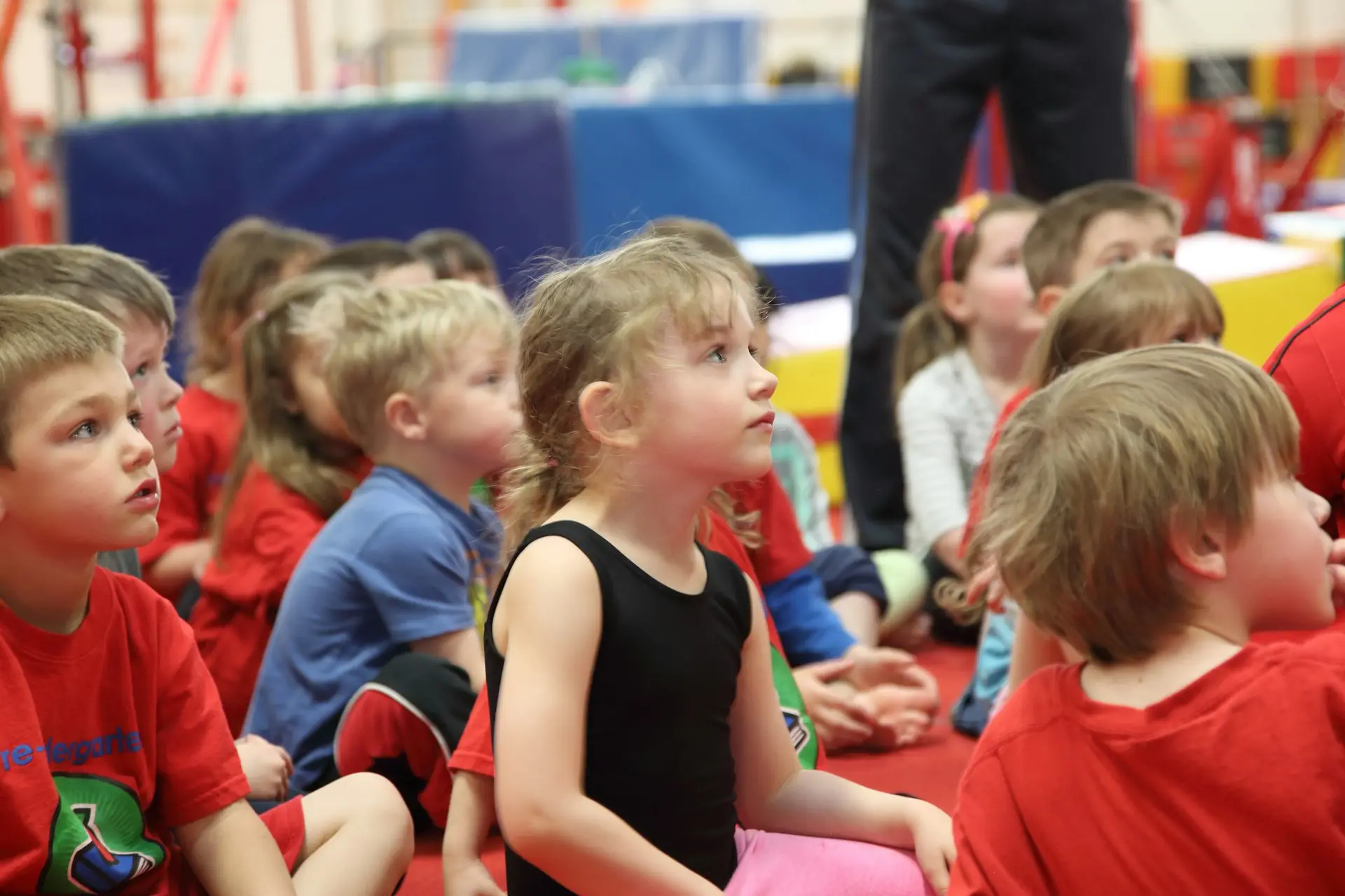 Kinder sitzen in einer Turnhalle auf dem Boden und hören aufmerksam zu