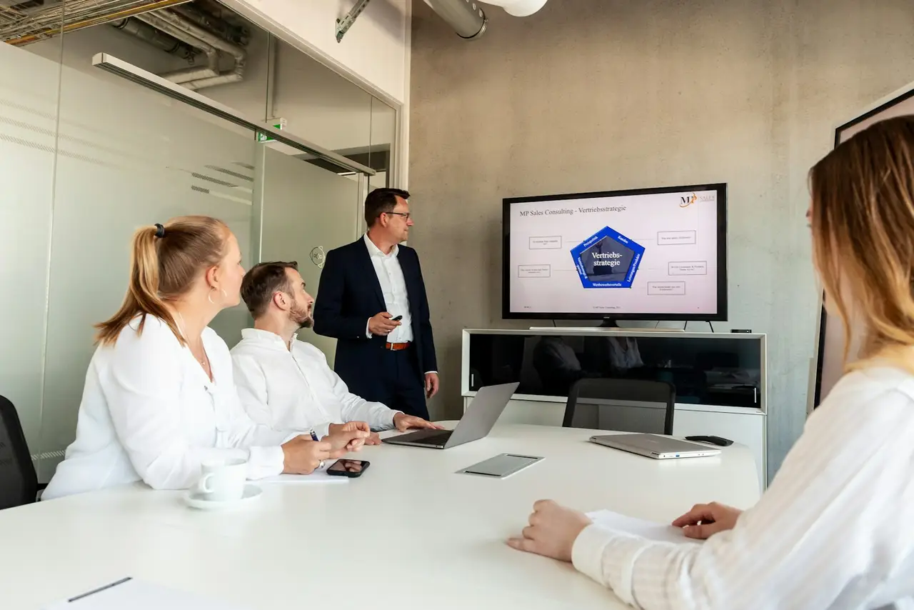 A presenter reviewing figures with colleagues in a conference room.