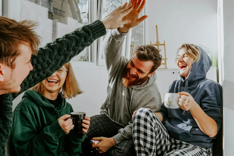 Four friends laughing and high-fiving over coffee
