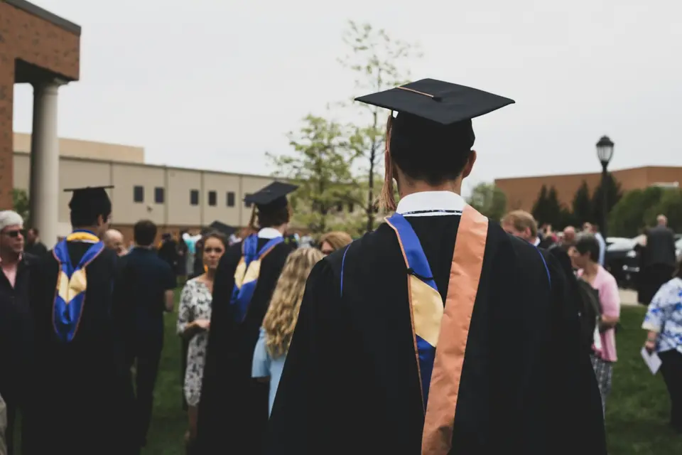 A graduate in cap and gown looking out over a campus gathering.