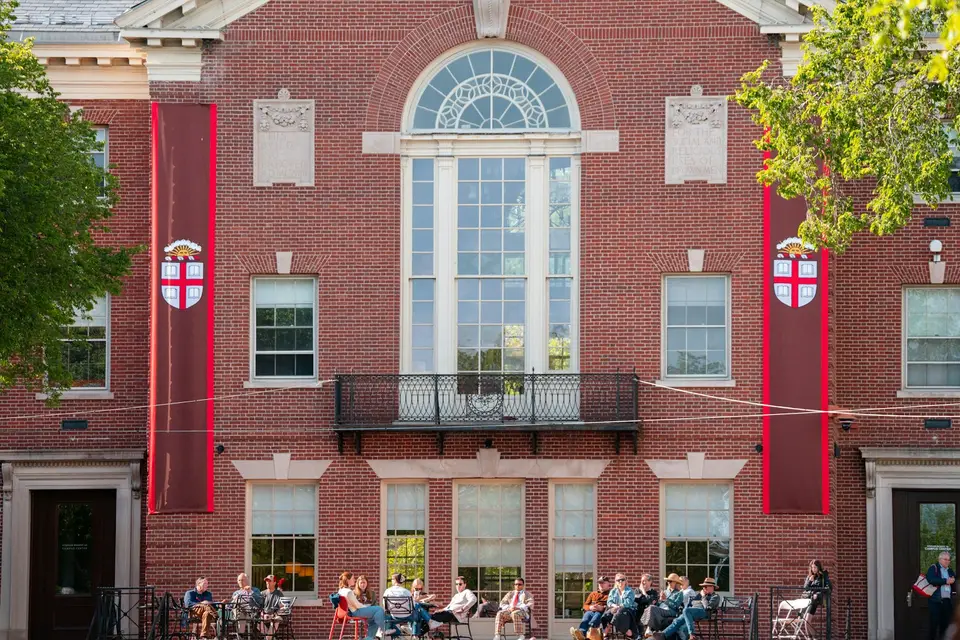 A brick campus building with banners and people on the lawn.
