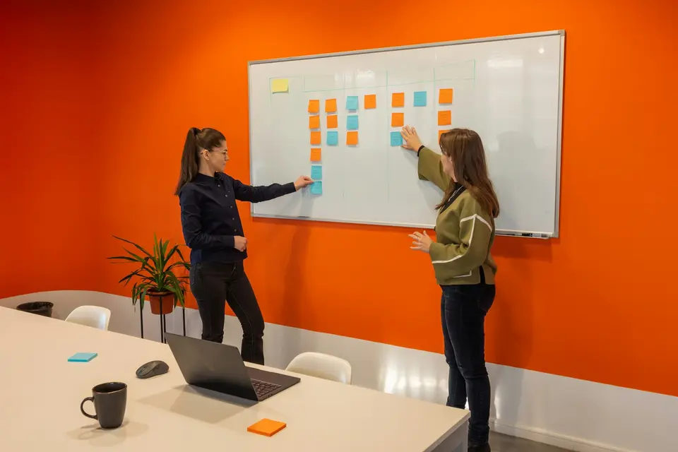 Two women discussing a plan in front of a whiteboard