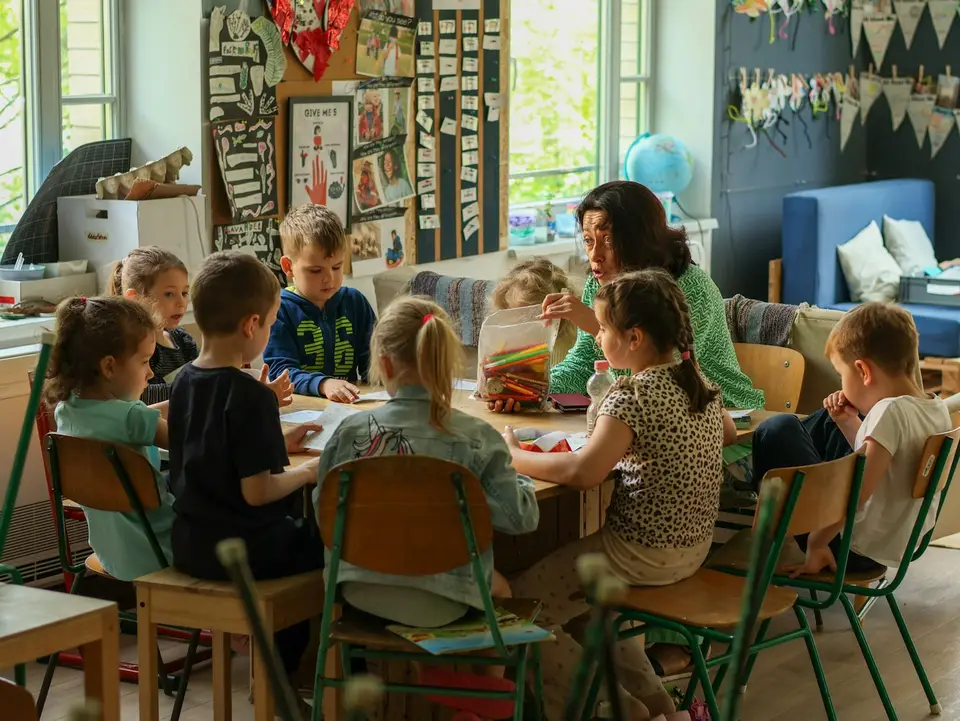 Children working at tables in a classroom with their teacher.
