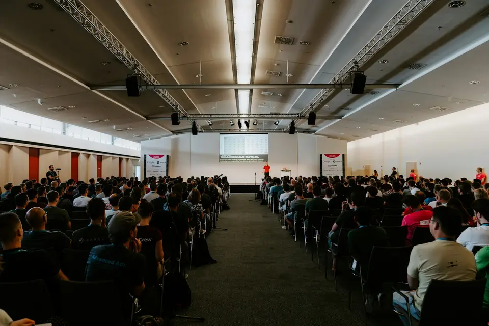 A large audience seated in a convention hall facing the stage.