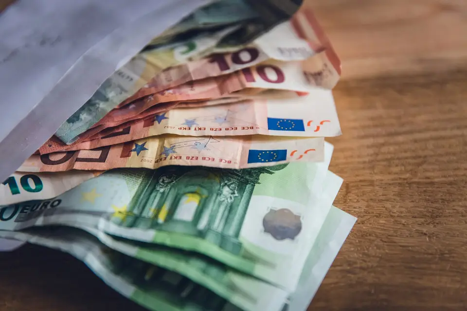 Euro-Banknoten ragen aus einem Briefumschlag auf einem Holztisch
