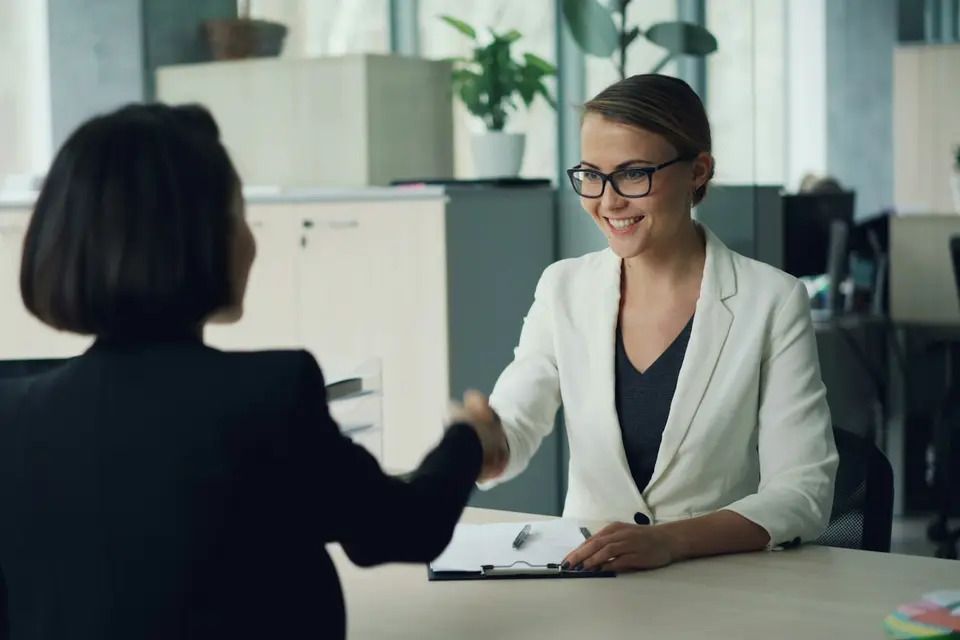 Two women shaking hands across a desk