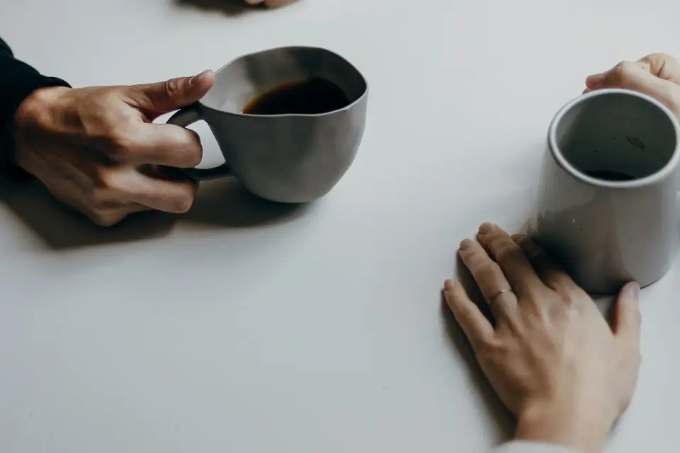 Zwei Personen sitzen sich bei einer Tasse Kaffee an einem hellen Tisch gegenüber