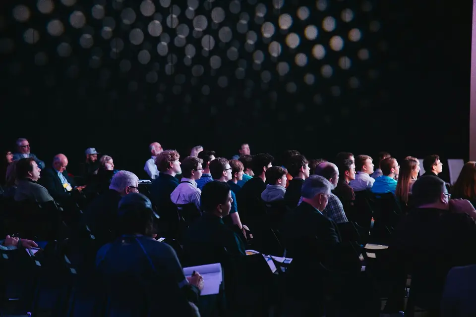 Zuhörende sitzen in Stuhlreihen in einem Saal