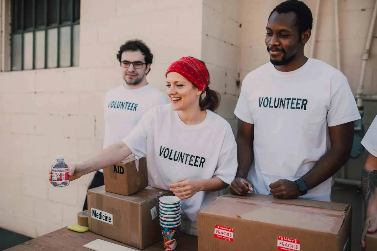 Drei Personen mit Kartons, die mit einem Volunteer T-Shirt Wasser ausgeben.