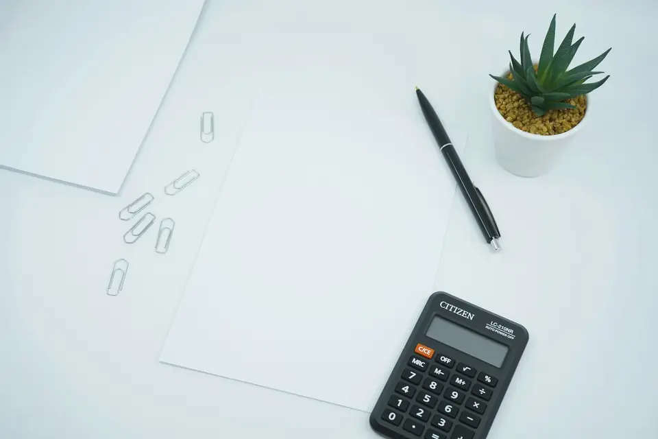 Calculator next to a pen on a white surface