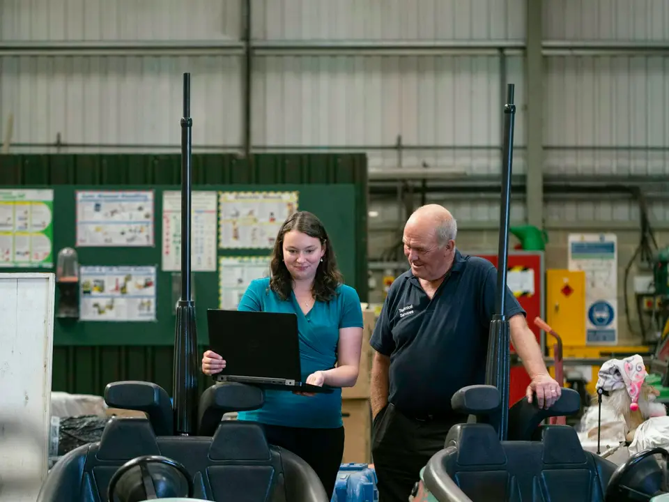 Two colleagues reviewing details on a laptop in a production facility.