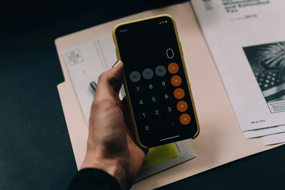 Hand hält ein Smartphone mit Taschenrechner über einen Ordner