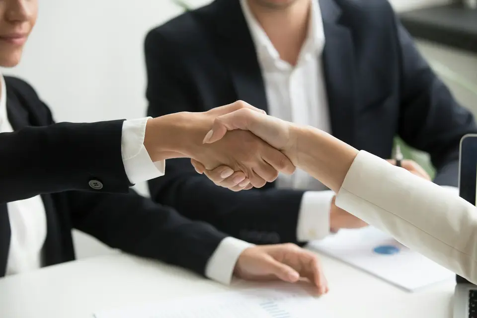 Zwei Personen geben sich am Besprechungstisch die Hand.