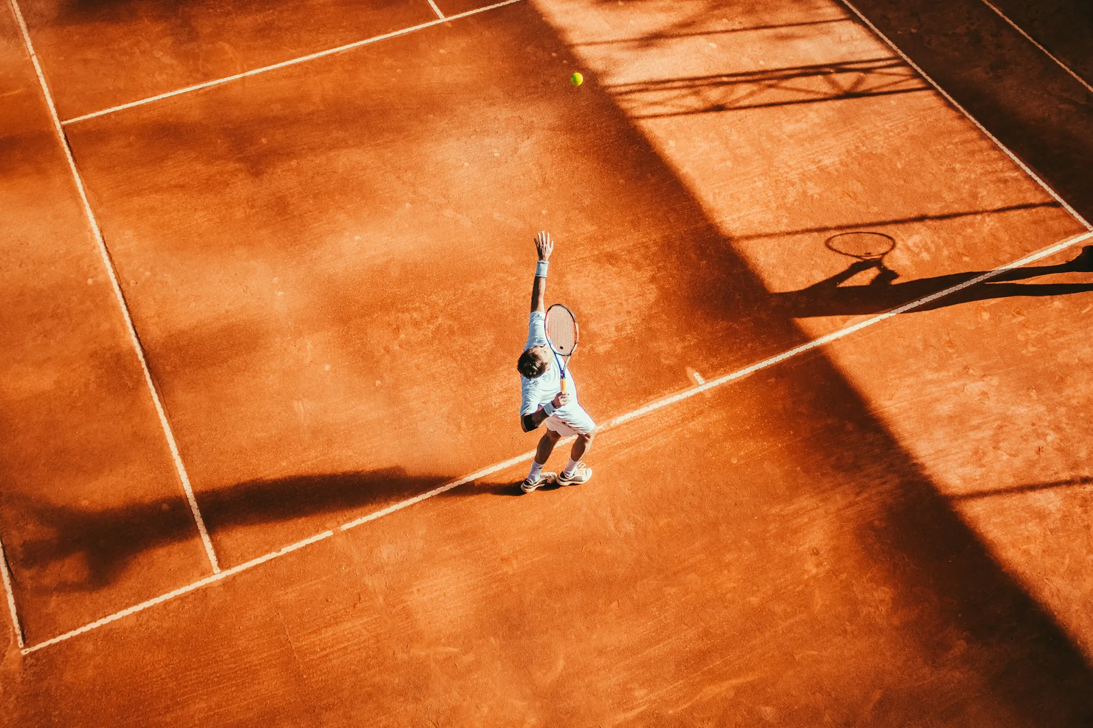 Ein Tennisspieler schlägt auf einem Sandplatz von oben gesehen auf.