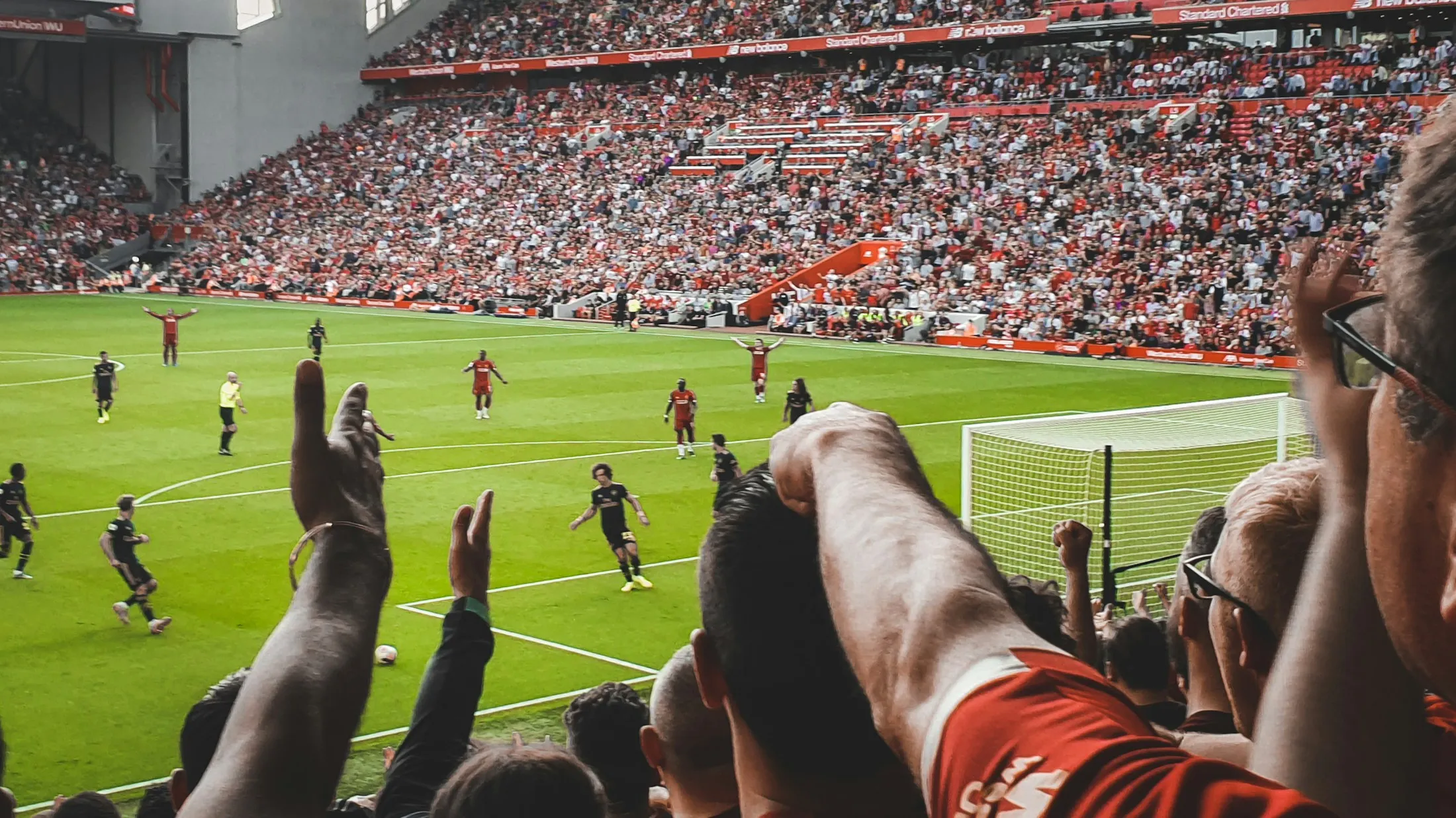 Fans recken im Stadion die Arme in die Höhe, während unten gespielt wird.