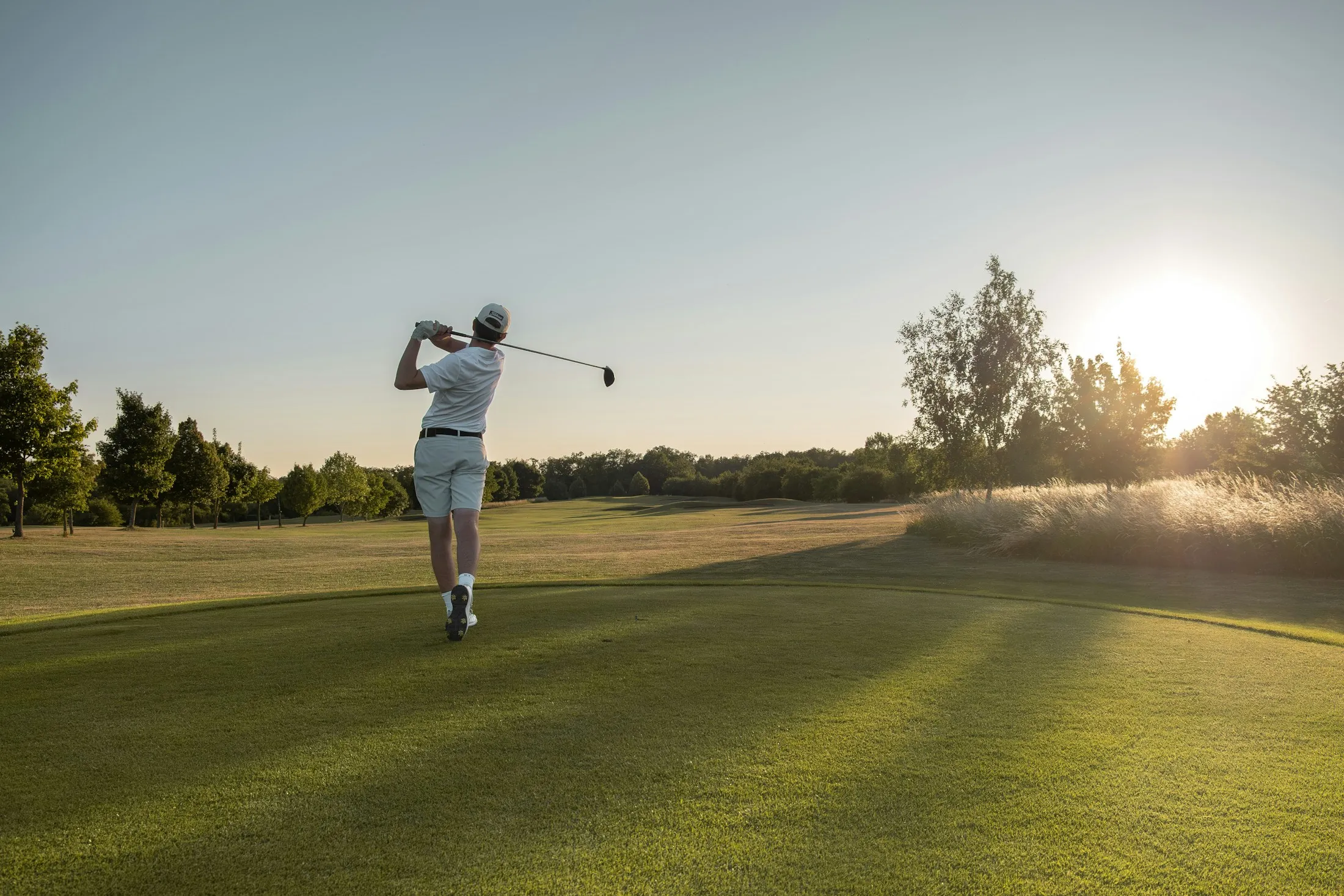 Ein Golfer schlägt bei tief stehender Sonne ab.