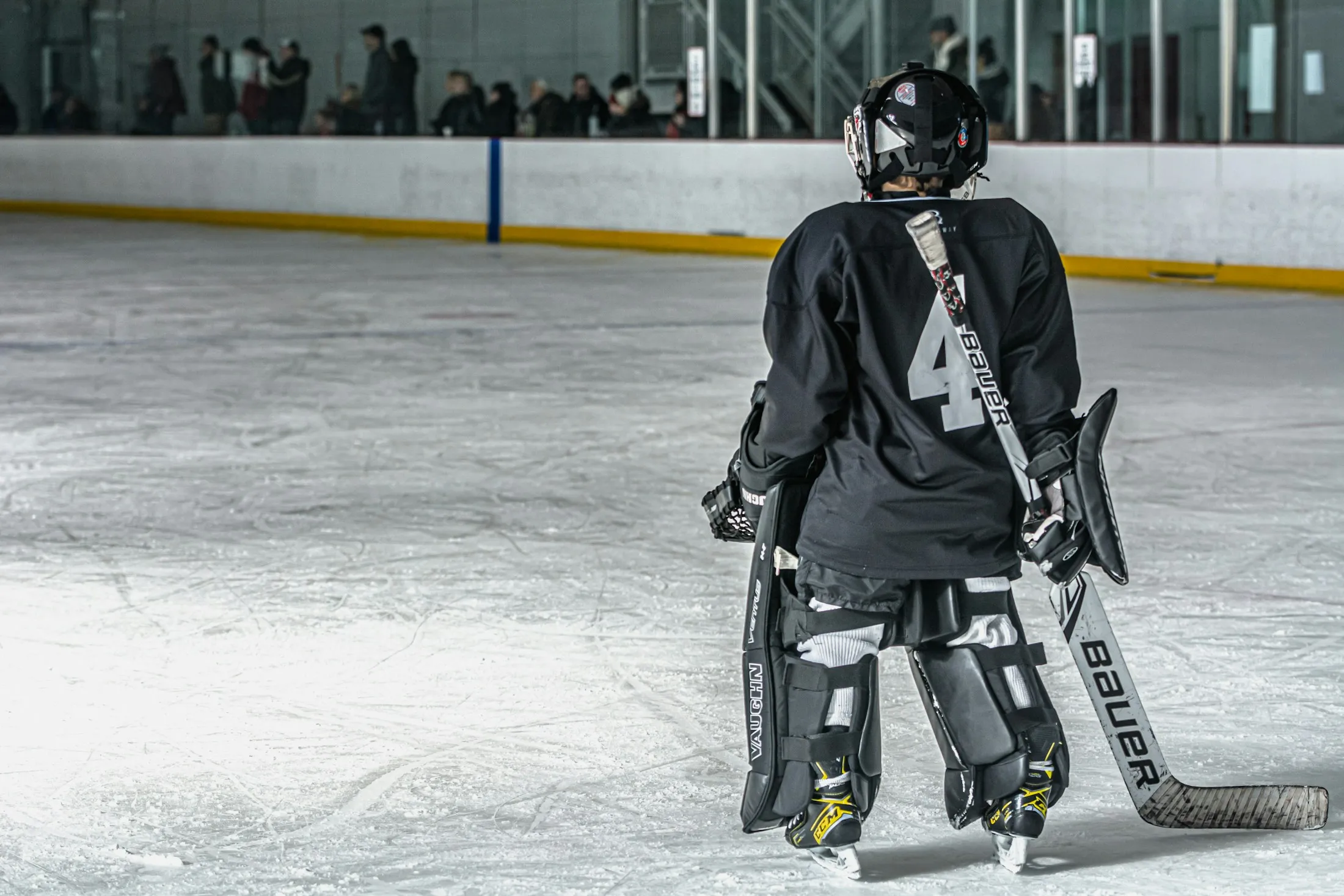 Ein Eishockeytorwart steht mit dem Rücken zur Kamera auf der Eisfläche.