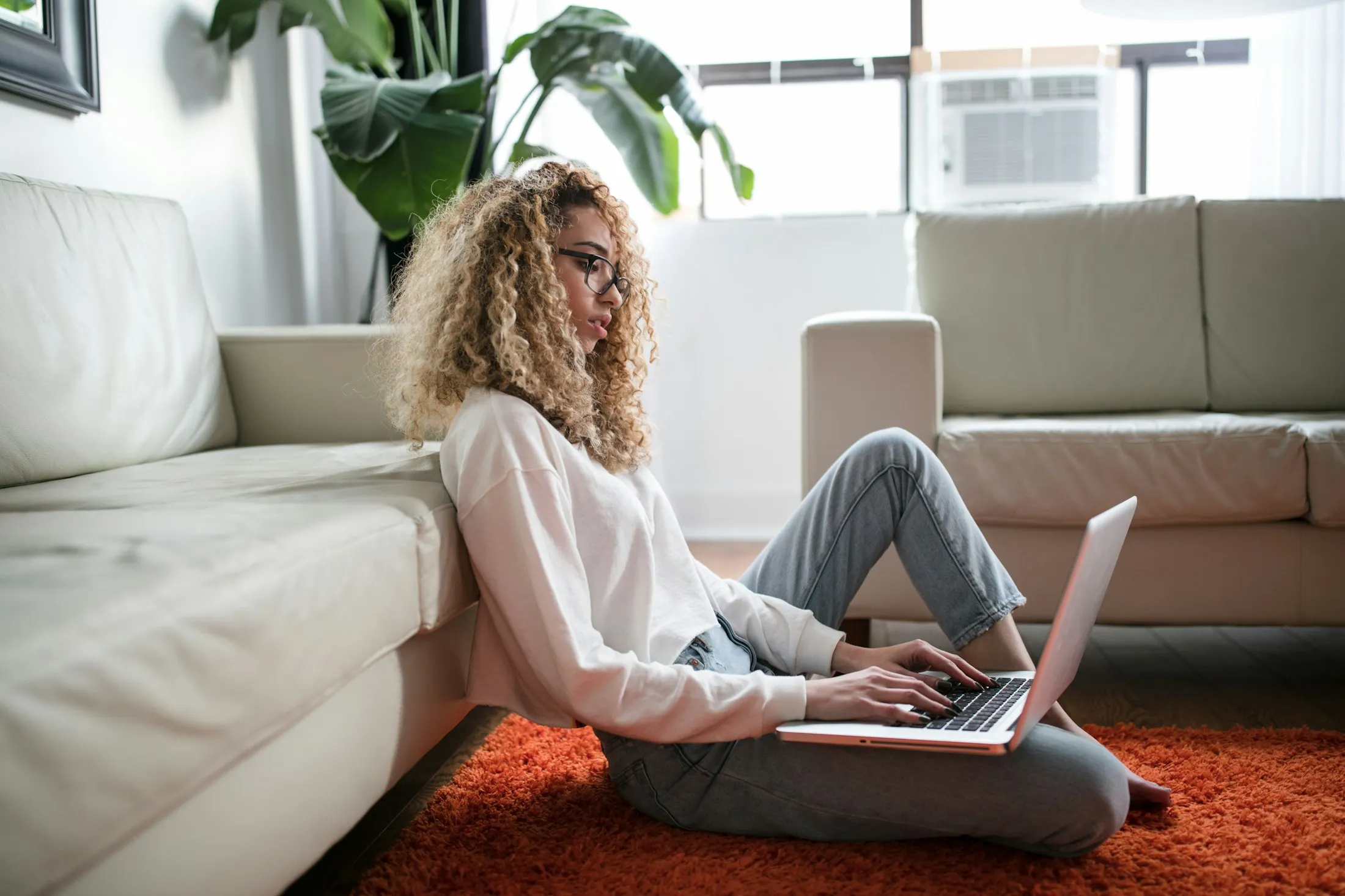 Eine Frau sitzt auf dem Boden und arbeitet an ihrem Laptop.