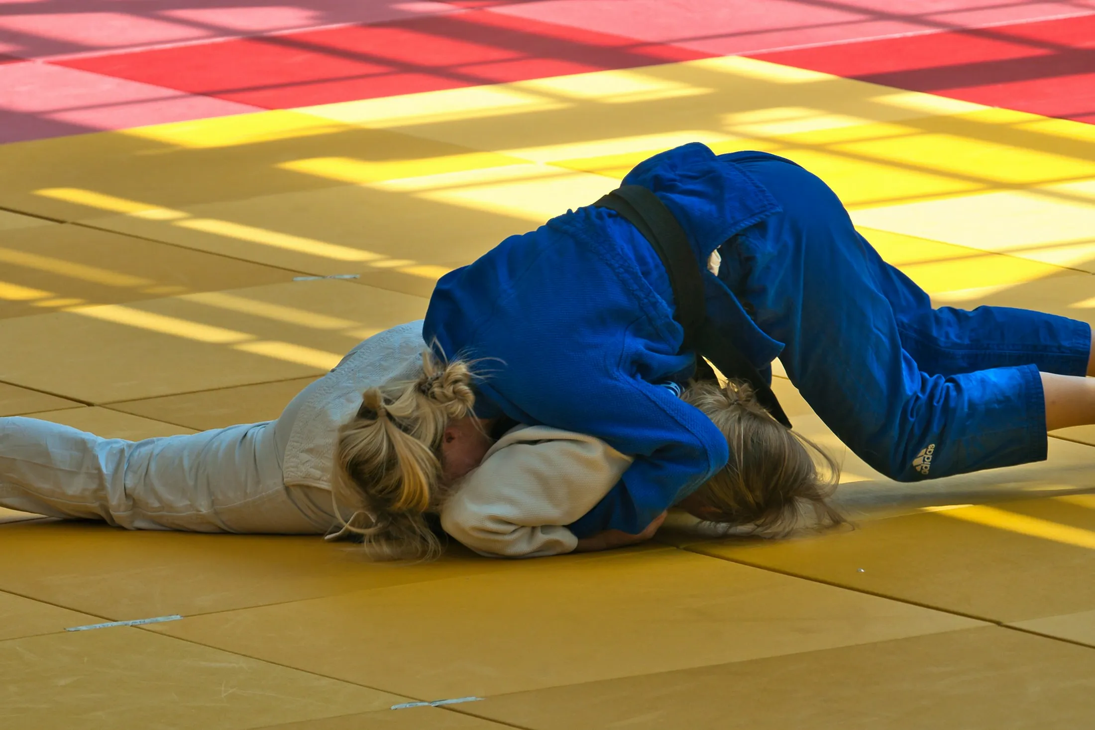 Zwei Judoka ringen auf einer gelben Matte am Boden.