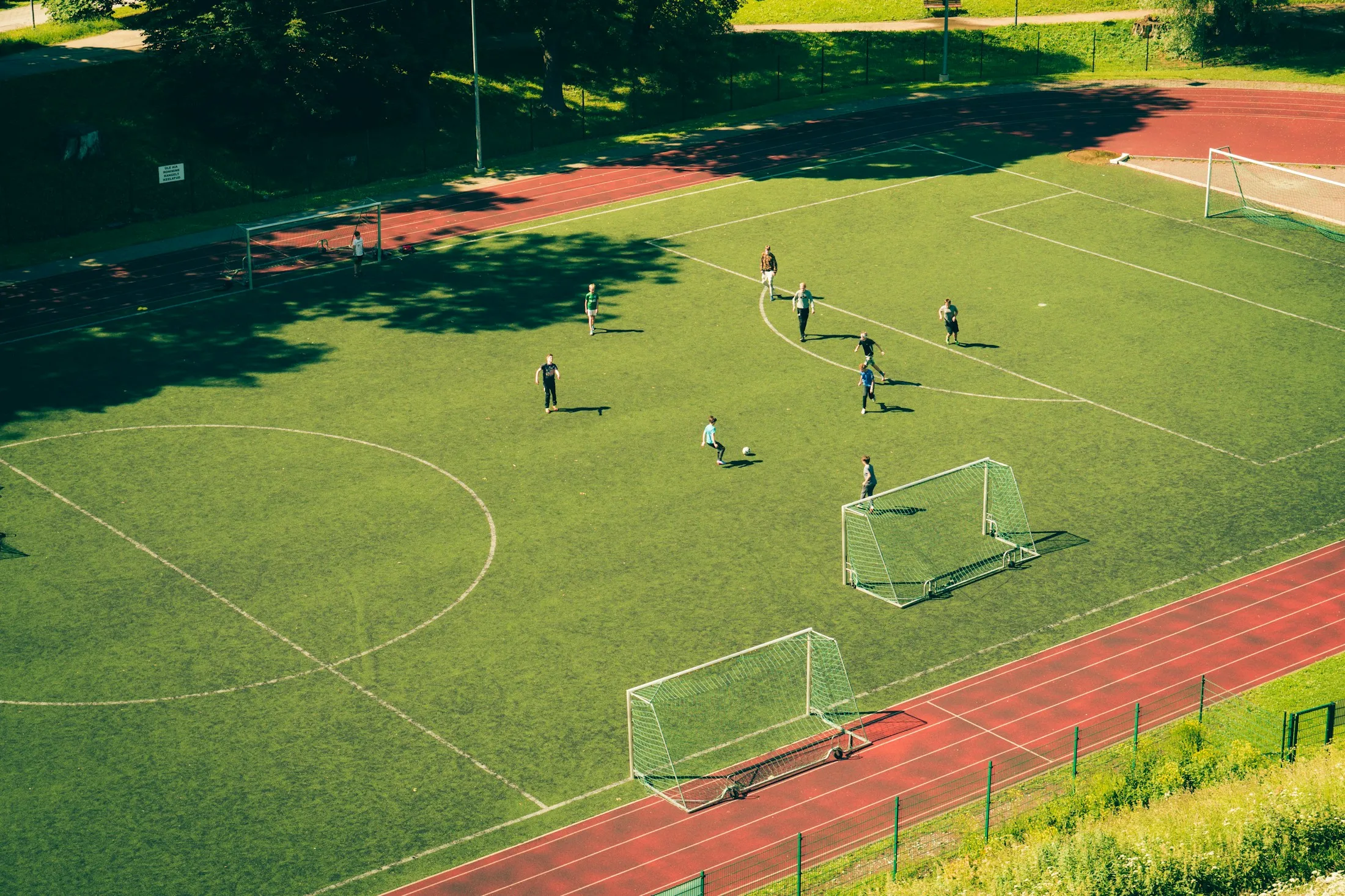 Ein Fußballplatz mit Laufbahn liegt von oben gesehen im Sonnenlicht.