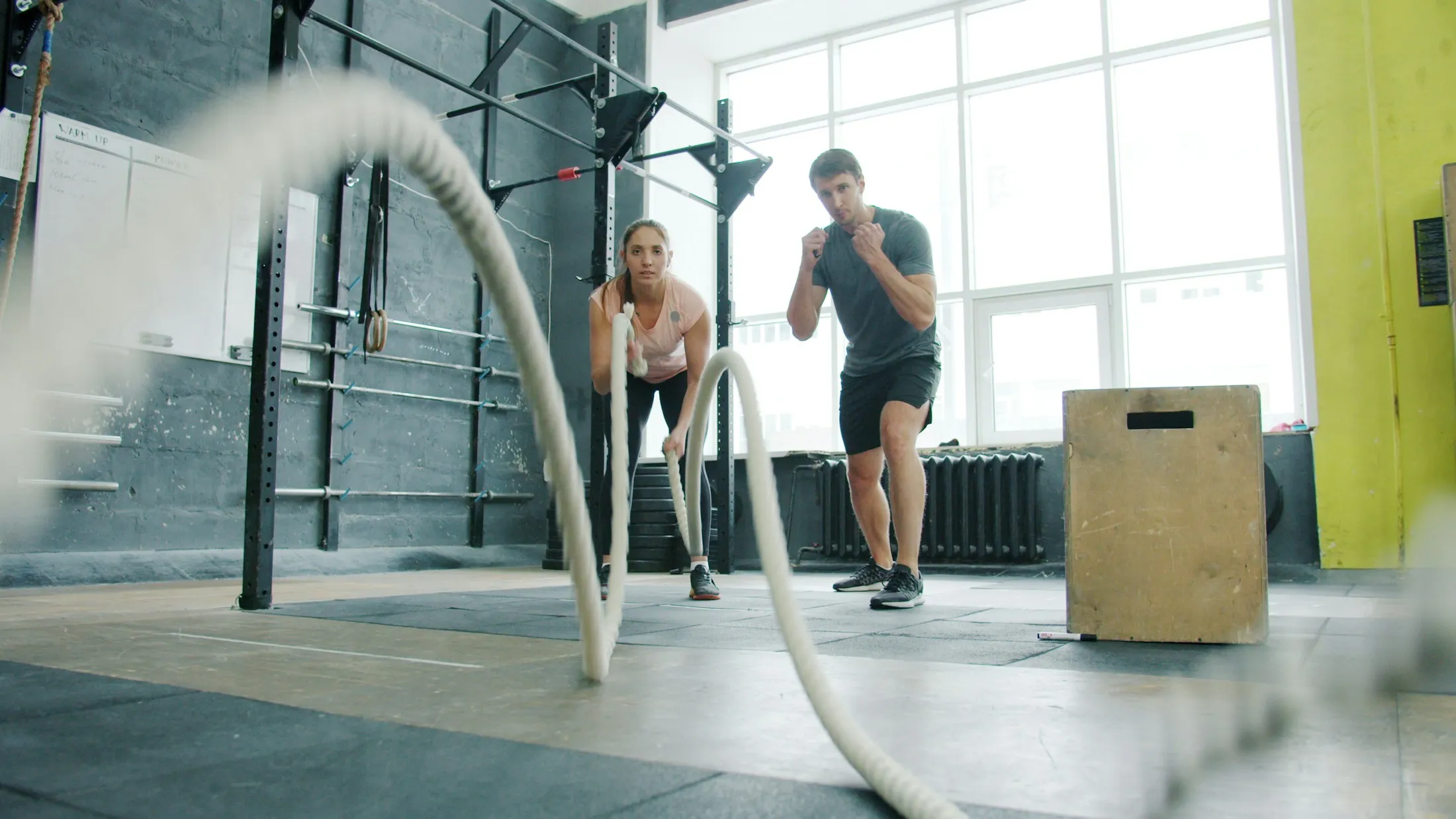 Eine Athletin trainiert mit Battle Ropes, während ein Coach zusieht.