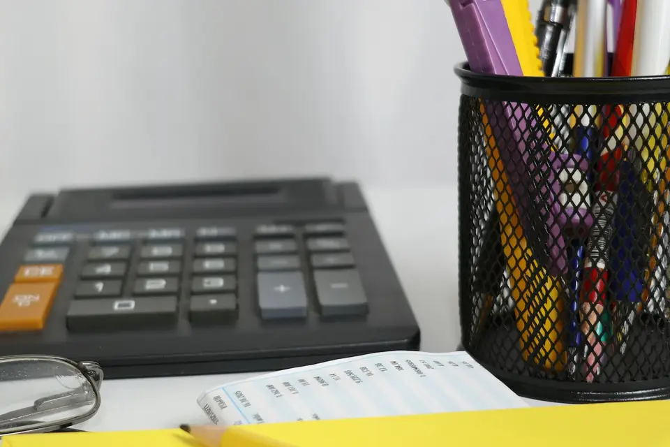 Taschenrechner, Stiftebecher und Belege auf einem hellen Schreibtisch