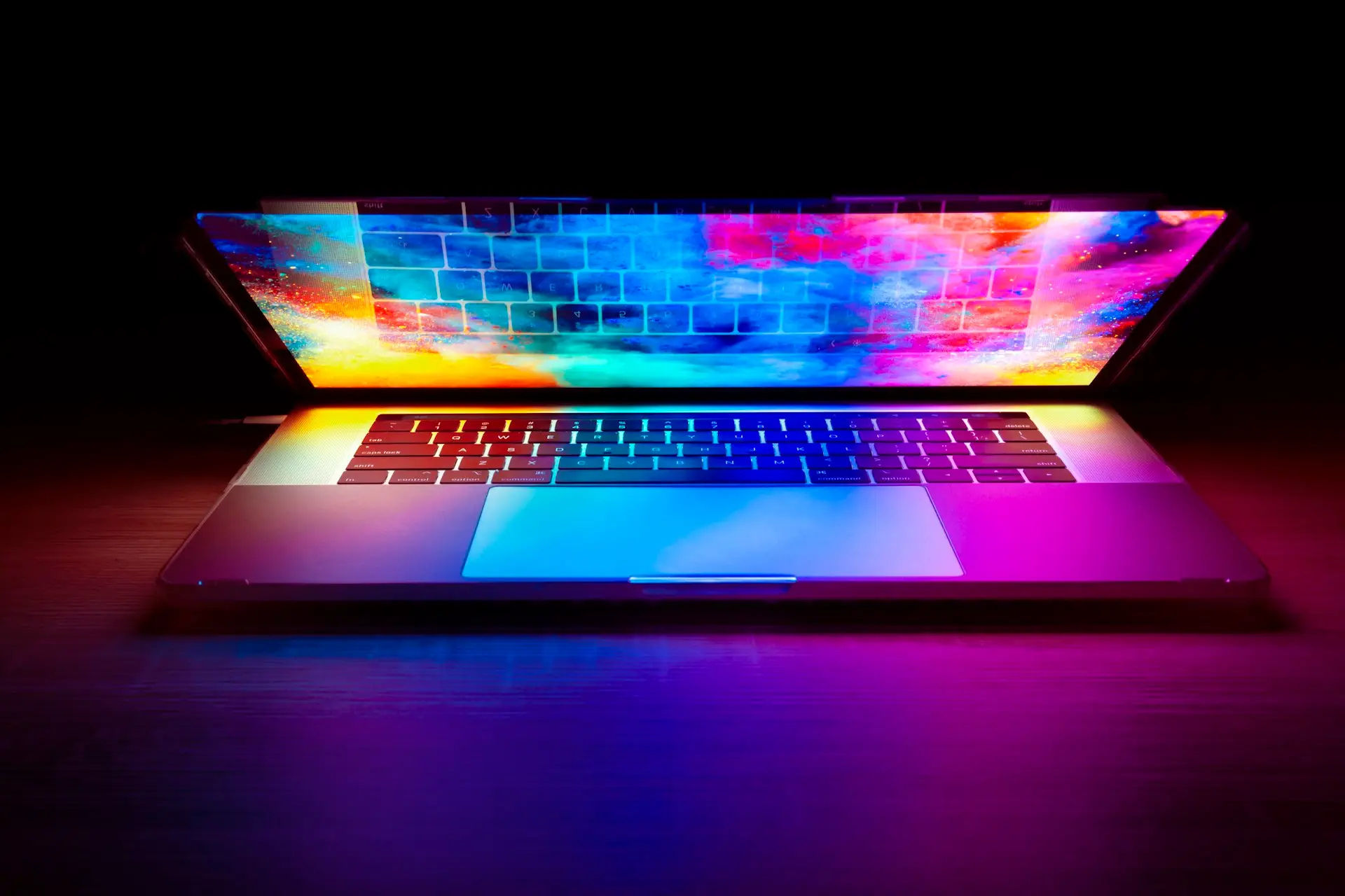 Aufgeklappter Laptop mit farbig leuchtendem Bildschirm in einem dunklen Raum