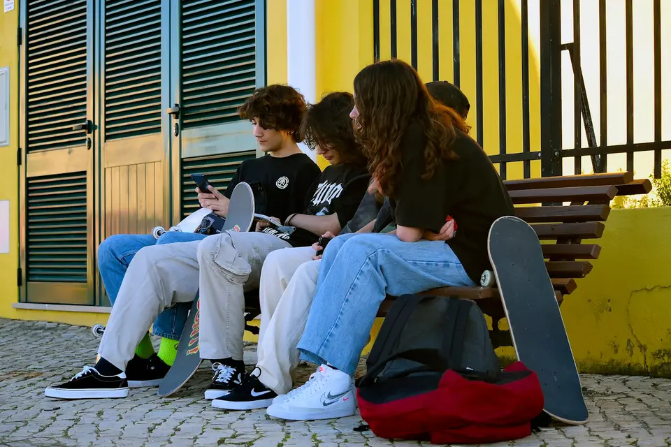 Jugendliche sitzen mit Skateboards auf einer Bank und schauen auf ihre Smartphones