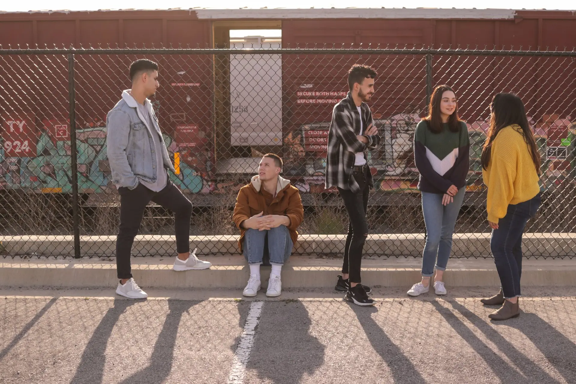 Fünf junge Leute stehen und sitzen im Gespräch vor einem Zaun