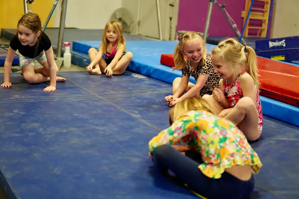 Fröhliche Kinder sitzen in einer Turnhalle auf blauen Matten