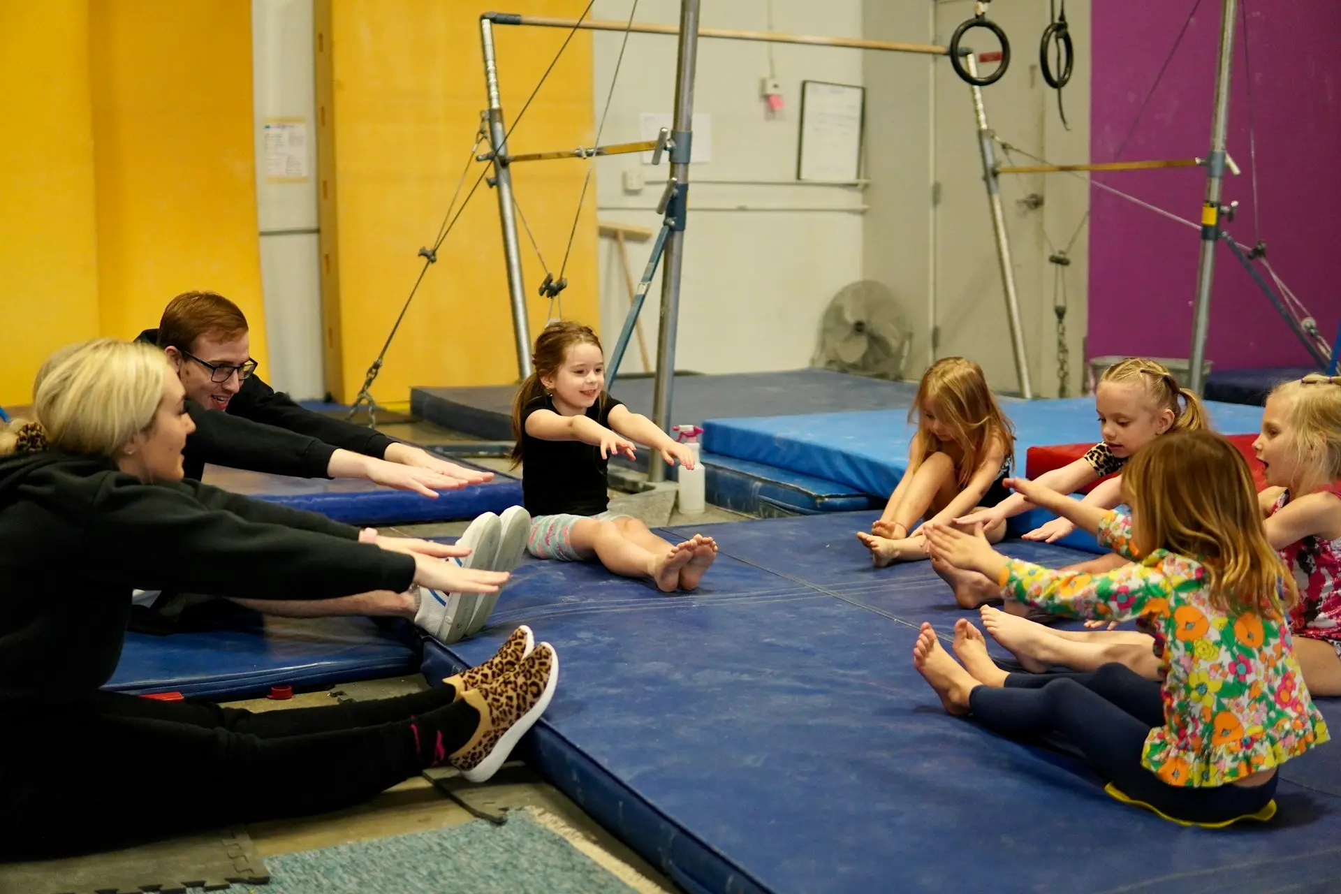 Kinder und Übungsleitende dehnen sich gemeinsam auf Turnmatten in einer Halle