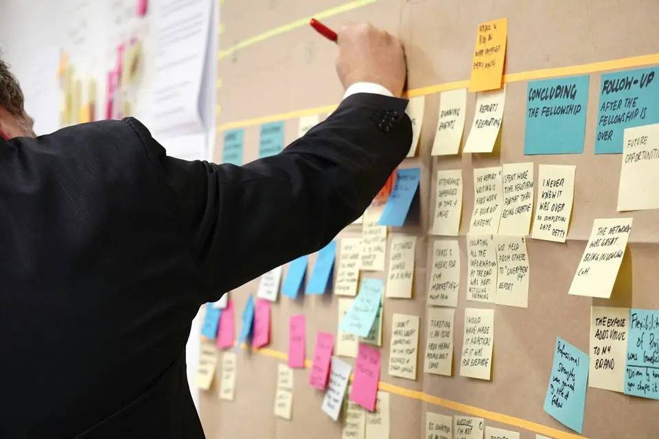 Ein Mann ordnet an einer Pinnwand voller Haftnotizen Ideen aus einem Workshop
