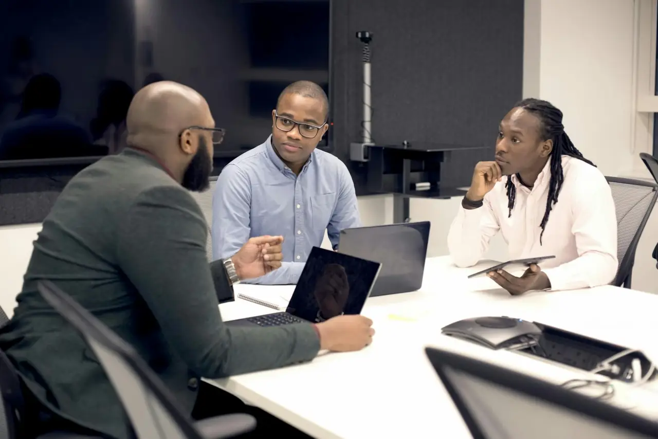 Three professionals discussing plans at a meeting table with laptops.