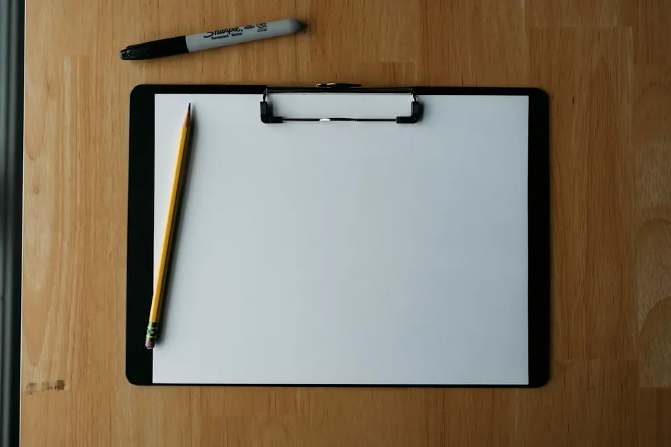 Leeres Klemmbrett mit Bleistift und Filzstift auf einem Holztisch