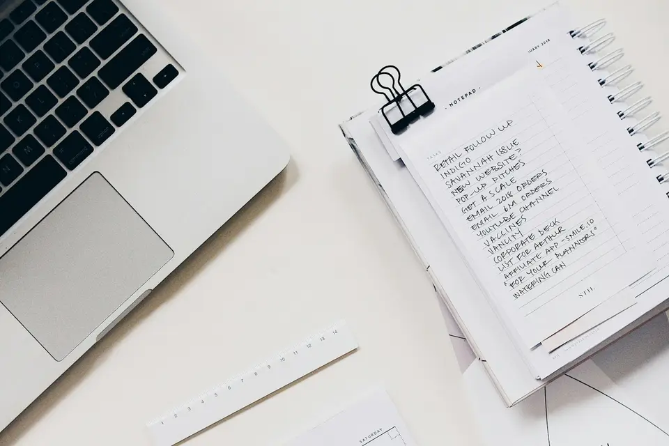 Laptop neben einer Notizbuchseite mit handschriftlicher Aufgabenliste