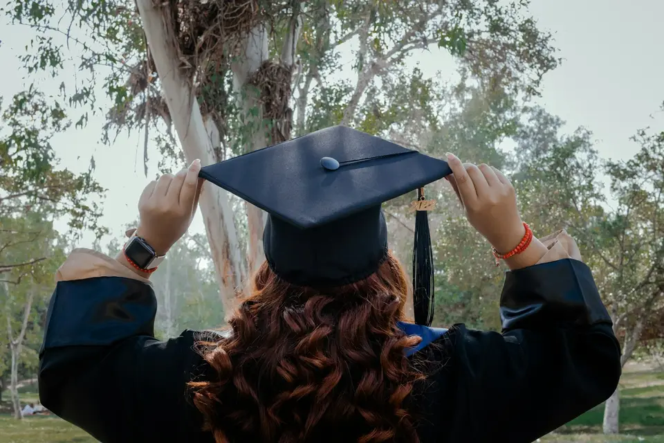A new graduate adjusting her cap outdoors.