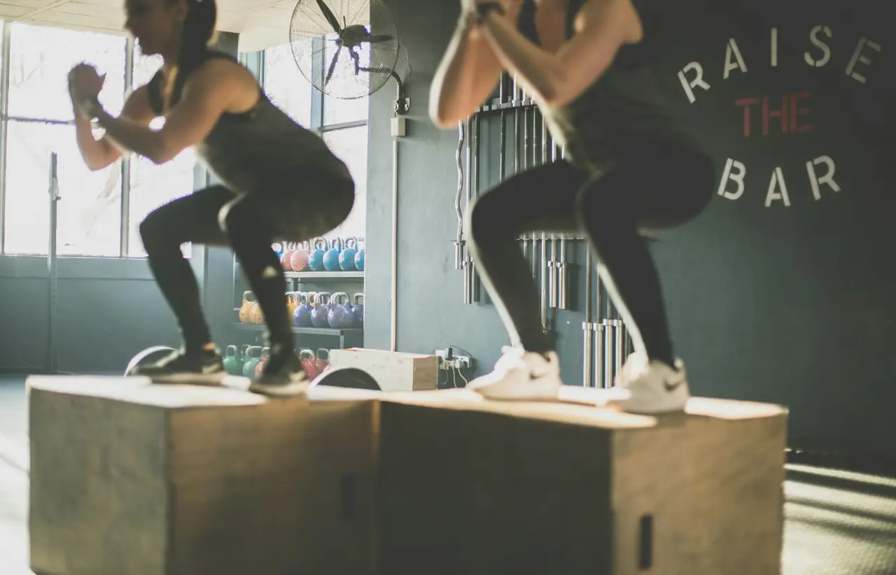 Zwei Athletinnen springen gemeinsam auf Holzboxen.
