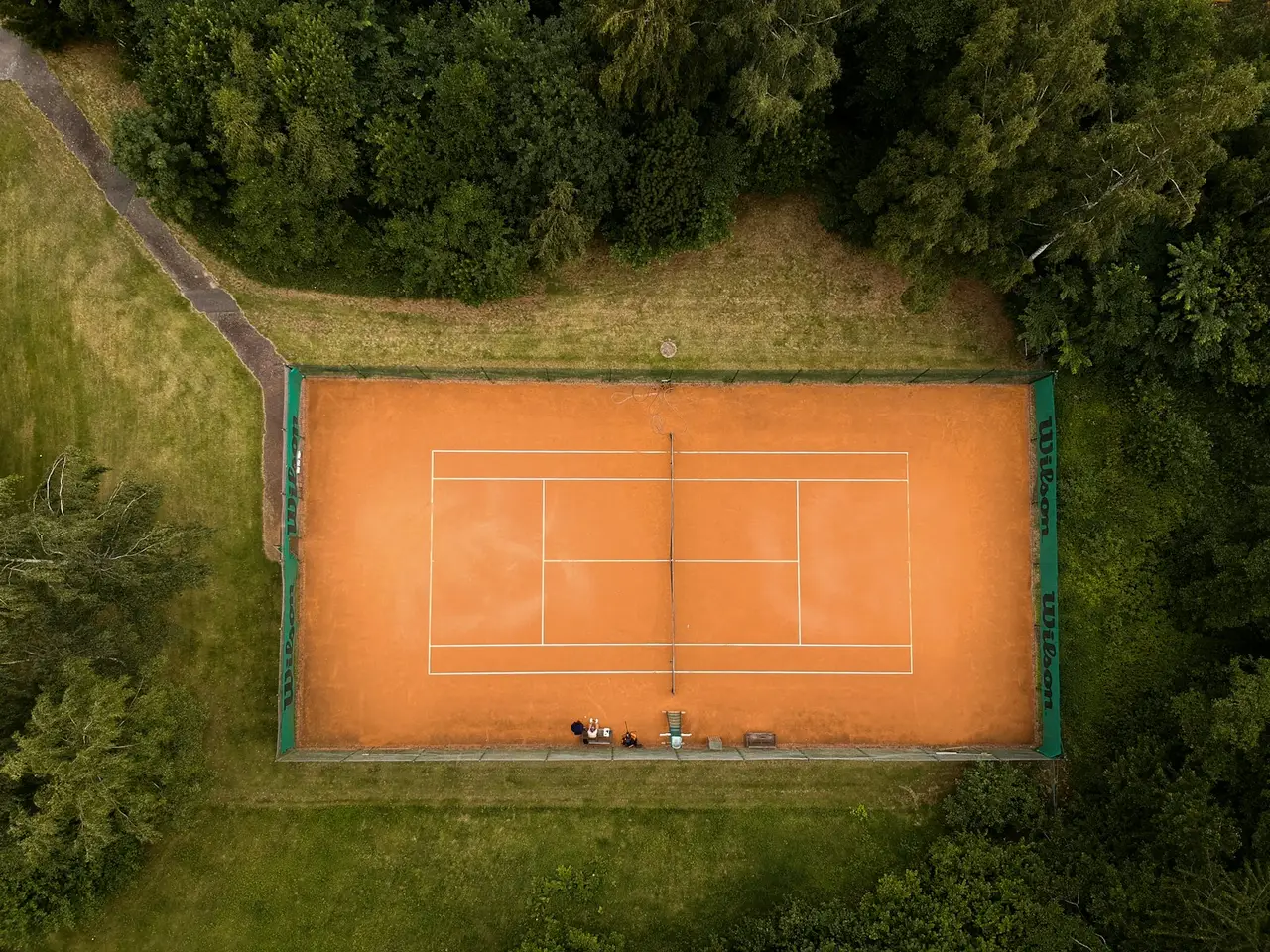 Ein Sandplatz liegt von oben gesehen zwischen Bäumen.